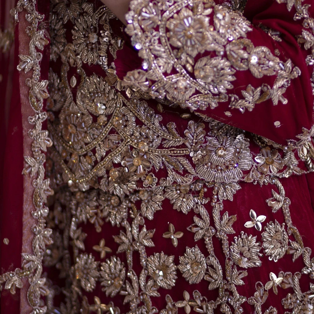 Close-up of zardozi embroidery with gold and silver threads, pearls, and crystals on a deep red bridal fabric.