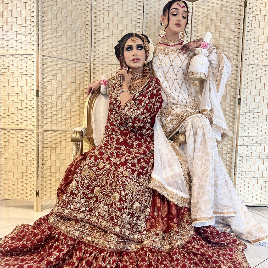 A model in a white lehenga with gold zari embroidery holding a bouquet, paired with a pearl-studded dupatta and Western-style tiara.