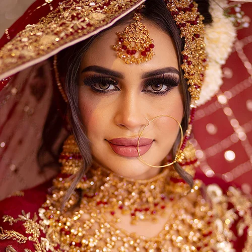 • A bride with bold emerald eyeshadow blended with gold shimmer, winged eyeliner, wispy lashes, and soft matte red lips.