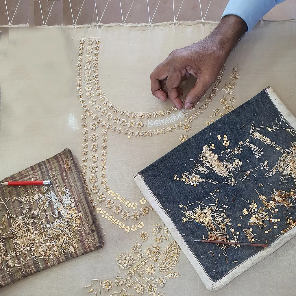 Close-up shot of artisans embroidering bridal fabric — threads of gold, mirrors, and beads in progress — showing authenticity and human craftsmanship.
